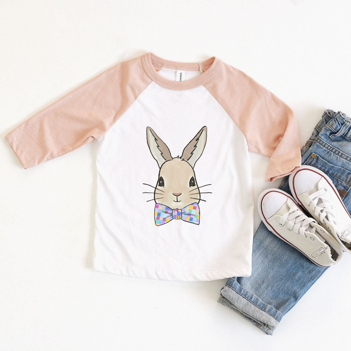 White raglan with peach sleeves and a graphic of a bunny wearing a bow tie with multicolored squares on it. 