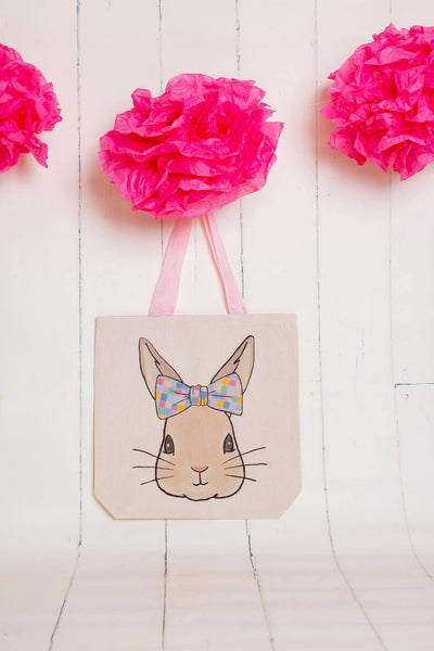 A canvas tote with pink handles and a graphic of a bunny wearing a bow with multi colored squares on it 