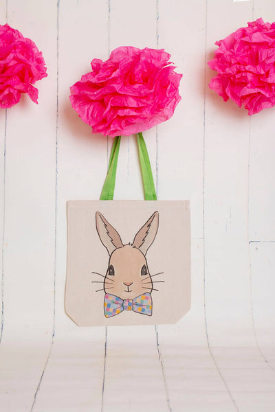 A canvas tote with green handles and a graphic of a bunny wearing a bowtie with multicolored squares on it 