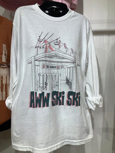 White long sleeve shirt with a ski shack and ski lift on it with mountains in the background under the graphic is text that says Aww Ski Ski with a peach shadow 