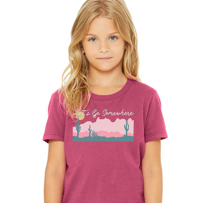 Heather Berry Shirt with graphic. Graphic is of a desert scene. Foreground is turquoise withe a dark pink as the mid ground and light pink on the horizon and a yellow sun. On top of the graphic are the words Let's Go Somewhere in a white cursive font with a turquoise shadow.